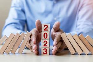 Businessman hand Stopping Falling of 2023 wooden Blocks. Business, Risk Management, Insurance, Resolution, strategy, solution, goal, New Year New You and happy holiday concepts photo