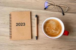 2023 cuaderno y taza de café sobre mesa de madera, vista superior y espacio para copiar. navidad, feliz año nuevo, objetivos, resolución, lista de tareas, estrategia y concepto de plan foto