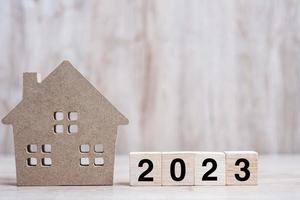 2023 Happy New Year with house model on table wooden background. Banking, real estate, investment, financial, savings and New Year Resolution concepts photo