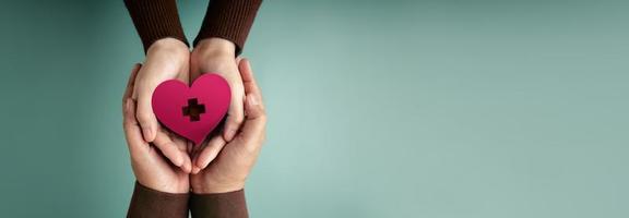 Donation Concepts. Hands of Volunteer People Embracing a Heart Shape with a Red Cross Sign Together. Love, Health Care, Donation and Charity. Top View photo