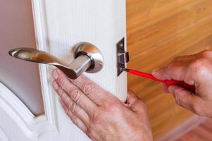 carpenter repairs the front door lock. fastens the handle with a screwdriver. photo