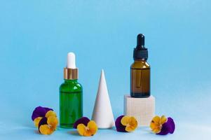 Serum glass bottles with pipette and beautiful viola flowers on blue background. Natural Organic Spa Cosmetic concept. Front view. photo
