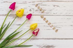 tulipanes rosados y amarillos sobre fondo de madera. tarjeta de felicitación de primavera con espacio de copia. cita de buenos dias foto