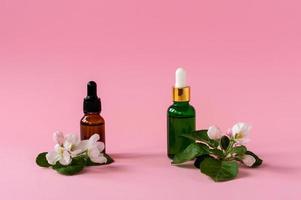 natural skincare bottle container with green leaf , flowers ingredients on pink background. Home made remedy and beauty product concept. photo