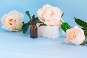 Two glass bottles with natural essential oils on a white podium with a peony flower. Cosmetic product on white geometric podium. Natural organic self care products photo