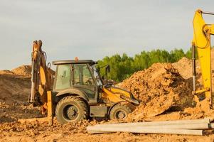 Yellow excavator during earthworks at construction site. Backhoe digging the ground for the foundation and for laying sewer pipes district heating. Earth-moving heavy equipment photo