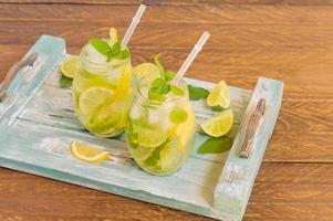 summer fresh cold lemonade with lime, lemon, mint and ice served on blue wooden tray. Non-alcoholic beverage photo