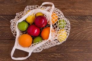 Organic fruits assorted in cotton mesh on wooden table, reusable shopping bag. sustainable lifestyle and zero waste concept. Copy space for text photo