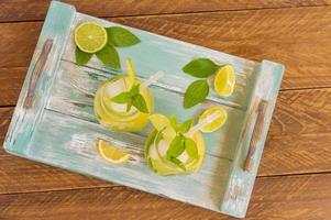 summer fresh cold lemonade with lime, lemon, mint and ice served on blue wooden tray. Non-alcoholic beverage photo