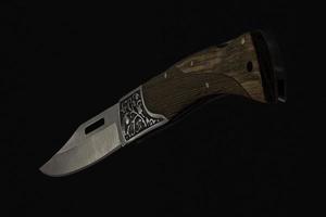close-up of foldable handmade knife with sharp blade, wooden handle on black background made in Cambodia photo