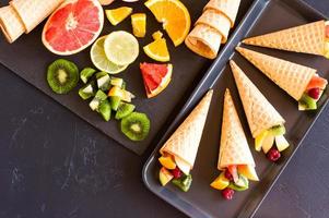 a mix of ripe cut fruit on a board and waffle cones for the holiday. top view. black background. photo