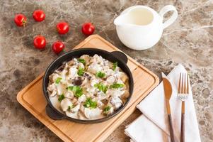 exquisite dish of white mushrooms in sour cream with spices in a frying pan on a marble background. photo