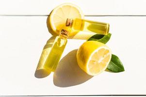 two transparent bottles with a cork lid with aromatic lemon oil on a white wooden table. sezhiy lemon and green leaves. sunlight. photo