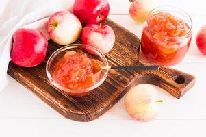deliciosa mermelada de manzana de manzanas jugosas en un frasco de vidrio y un recipiente para mermelada en una tabla de madera. foto