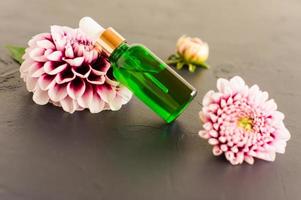 a bottle of green glass with cosmetic or essential oil for face and body care on a black background with a purple dahlia flower. photo