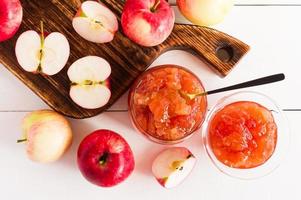 mermelada de manzana fragante y mitades de manzanas sobre una tabla de madera y un fondo blanco. vista superior. foto