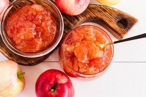 Deliciosa mermelada de manzana en un frasco de vidrio sobre el fondo de una mesa de madera blanca. foto