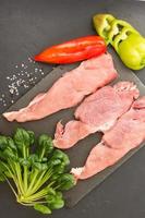 fresh farm meat on a slate board and a black background with vegetables and spinach greens. kind of svrhu. vertical image. photo