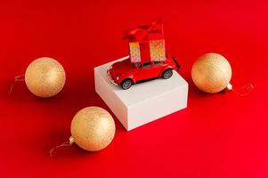 Red retro car with a gift box on the roof on a white pouill and a red background with a new-fashion ball. a copy of the space. photo