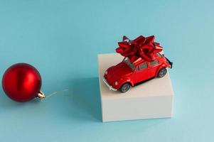 miniature model of a retro car of red color on a white pouill with a festive bow. New Year's blue background with a red ball. photo