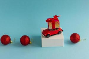 a miniature model of a red car with a New Year's gift on the roof against a blue background with three red balls. a copy of the space. photo