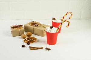 Christmas composition on a white background. gift boxes made of kraft paper and two paper red cups with cocoa and marshmallow. nuts, anise stars. photo