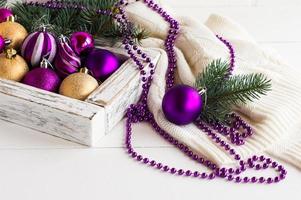 composición festiva de la reunión de año nuevo y navidad. caja de madera blanca con coloridos juguetes navideños, abalorios, suéter de punto. foto