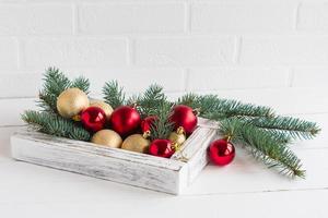 decorative white box made of wood with festive Christmas balls on a white wooden table on a white brick wall and spruce branches. photo