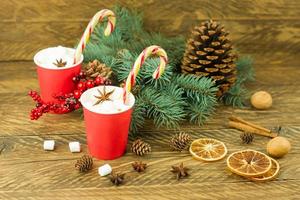 New Year's composition on a wooden background. two paper red cups with coffee and marshmallows, caramel, blue spruce branches and a cedar cone. photo