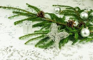 decoración de año nuevo de la casa con una rama verde de abeto con conos con bolas brillantes y mariposa plateada abierta. fondo de nieve blanca. foto
