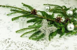 New Year's decoration of the house with a green branch of spruce with cones with shiny balls and openwork silver butterfly. white snow background. photo