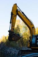 una excavadora de orugas amarilla espera la excavación en la carretera cerca del bosque de otoño temprano en la mañana. foto