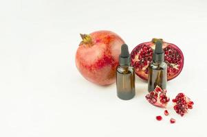 two glass bottles with a pipette with organic pomegranate seed oil on the background of the fruit of ripe pomegranate. moisturizing, aromatherapy. photo