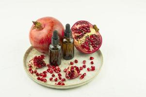 cosmetic oil of pomegranate seeds in bottles with brown glass droppers on a ceramic plate with pomegranate and fruit grains. photo