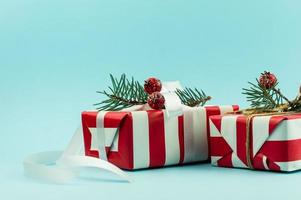 dos regalos festivos en envases rojos y blancos con elementos decorativos de ramas de abeto y bayas con una cinta blanca. fondo azul. foto