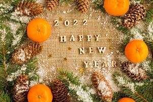fondo tradicional de año nuevo y navidad con los mejores deseos, con letras y números del próximo año. mandarinas, ramas de abeto, conos. foto