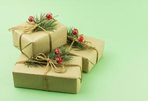 three boxes of gifts in craft paper with decor of spruce branches and berries on a green background. photo