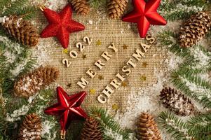 Merry Christmas and New Year 2022. festive background with red stars, snow-covered branches of spruce and cones on burlap. top view. photo