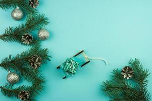 composición de año nuevo con ramas decoradas de bolas y conos de plata de abeto. trineo decorativo con un regalo sobre un fondo azul. copie el espacio foto