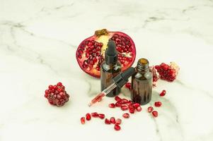 moisturizing oil fluid for the face with extract of pomegranate seeds on a marble background and pomegranate fruit. photo