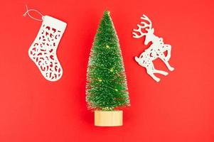 flat layout. top view. red New Year's background. green toy spruce with a garland of lights, white decorative deer and sock. photo