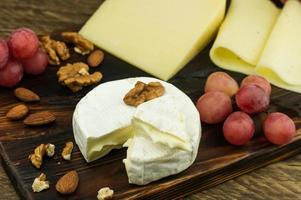 Camembert cheese with a white crust and a soft creamy structure on a wooden board with nuts and grapes. photo