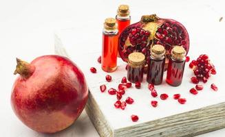 wooden white pedium with bottles of pomegranate essential oil and essence from pomegranate seeds. ripe pomegranate with grains. photo