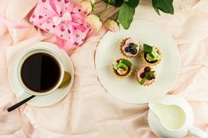 desayuno en la cama en st. dia de valentin una taza de café, una mini tortilla con crema y fruta. fondo rosa pastel. foto