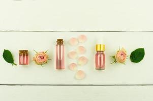 glass bottles with rose water and essential oil of rose petals, buds and green leaves on a white wooden background. flat lay. top view. photo