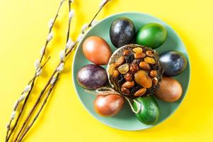 a festive plate with Treats for Easter. homemade cake with nuts and dried fruits, colorful eggs. yellow background. photo
