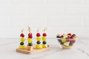 canapes of juicy fruit on a wooden board and a bowl with chopped fruit banana, pear, raspberry. delicious, healthy food photo