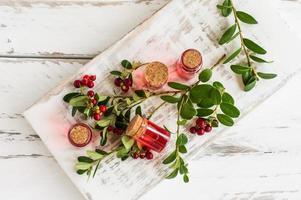 glass bottles with a cork lid of natural extract from cranberries on a white wooden rustic background. elixir of youth. photo