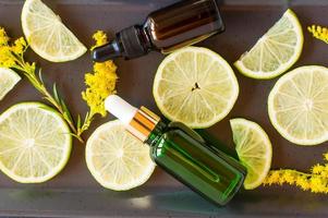 moisturizing oil-fluid for the face with citrus extract in bottles with a pipette against the background of slices of lemon and sprigs of solidago. photo