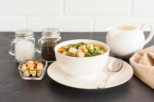 white mushroom soup with parsley, cream and croutons in a soup plate on a black background opposite a white brick wall. photo